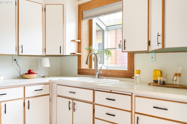 kitchen featuring light countertops, a skylight, a sink, and white cabinetry