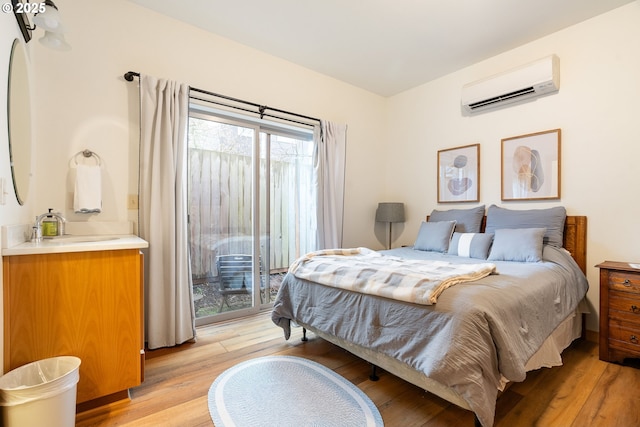 bedroom featuring an AC wall unit, light wood-type flooring, a sink, and access to exterior