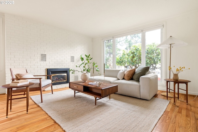 living area with visible vents, baseboards, light wood-style flooring, brick wall, and a brick fireplace