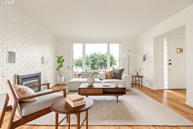 living room with visible vents, ornamental molding, a brick fireplace, wood finished floors, and baseboards