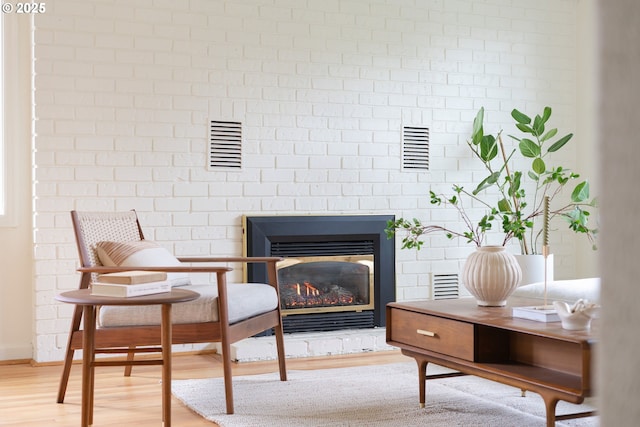 living area featuring light wood-type flooring, visible vents, and a brick fireplace