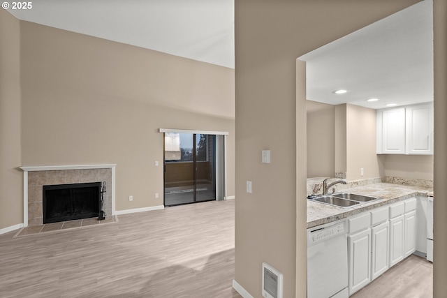 kitchen featuring white dishwasher, a fireplace, white cabinetry, and sink