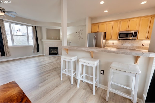 10955 SW 130th Ave, Tigard, OR 97223 - kitchen featuring stainless steel appliances, a breakfast bar area, tasteful backsplash, light wood-style flooring, and light brown cabinets