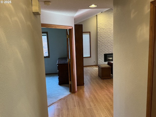 corridor featuring lofted ceiling, a textured ceiling, and light hardwood / wood-style flooring