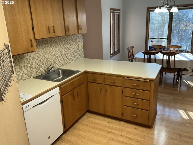 kitchen featuring sink, light hardwood / wood-style flooring, dishwasher, decorative light fixtures, and kitchen peninsula