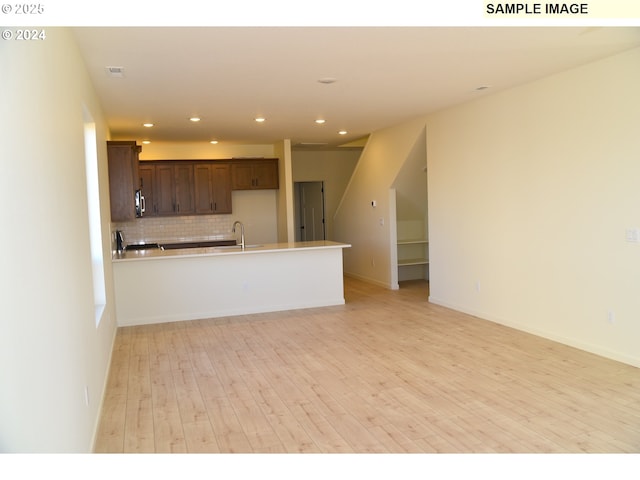 kitchen with recessed lighting, decorative backsplash, light wood-style floors, a peninsula, and open floor plan