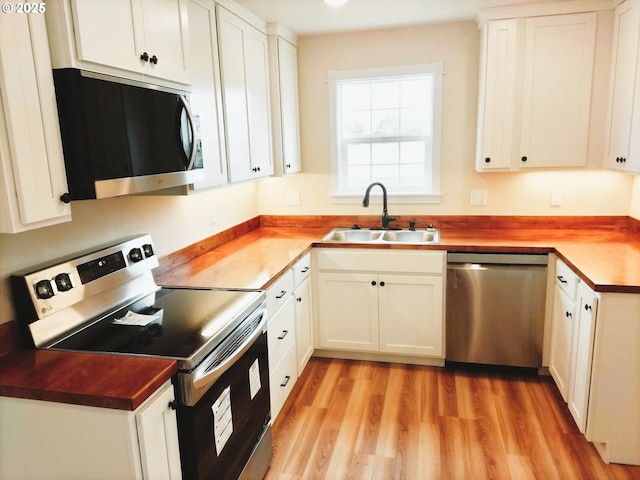 kitchen with light wood-type flooring, white cabinetry, a sink, wood counters, and appliances with stainless steel finishes