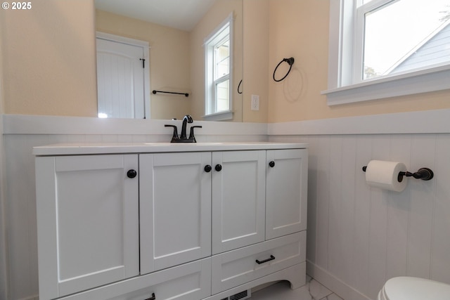 bathroom with vanity, toilet, marble finish floor, and a wainscoted wall