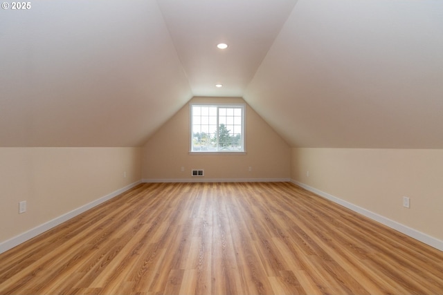 additional living space with baseboards, vaulted ceiling, light wood-style flooring, and visible vents