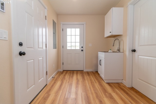 washroom featuring baseboards, a sink, electric panel, and light wood-type flooring
