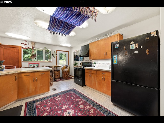 62242 Tamarack Springs Ln, Summerville, OR 97876 - kitchen featuring black appliances, wall chimney exhaust hood, tile counters, brown cabinets, and a textured ceiling