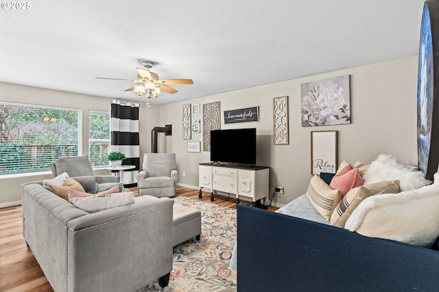 living room featuring ceiling fan, light hardwood / wood-style floors, a textured ceiling, and a wood stove