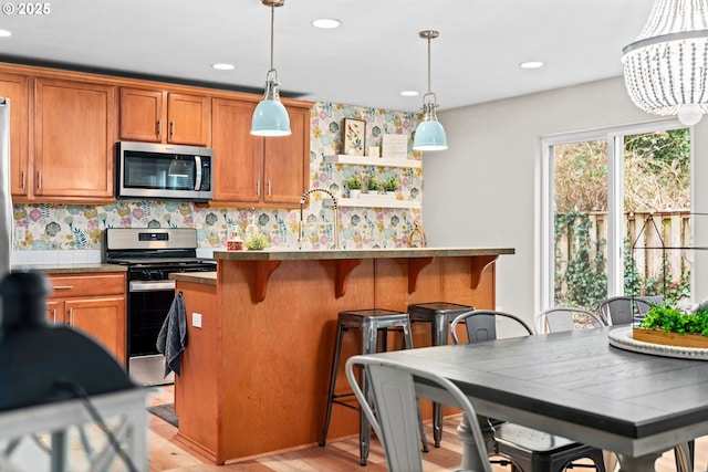 kitchen with decorative light fixtures, appliances with stainless steel finishes, a kitchen breakfast bar, light hardwood / wood-style floors, and backsplash