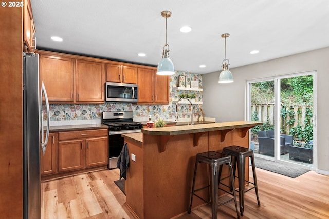 kitchen featuring decorative light fixtures, stainless steel appliances, light hardwood / wood-style floors, and a center island with sink