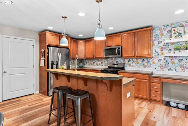 kitchen featuring a kitchen bar, light hardwood / wood-style flooring, hanging light fixtures, a center island with sink, and stainless steel appliances