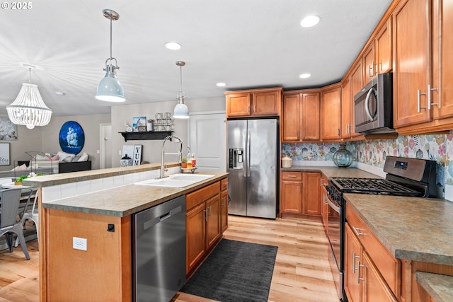 kitchen featuring pendant lighting, sink, appliances with stainless steel finishes, a center island with sink, and light wood-type flooring