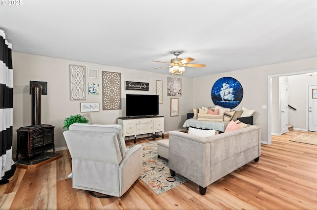 living room featuring light hardwood / wood-style flooring, ceiling fan, and a wood stove