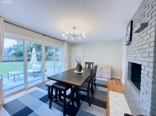 dining room with light wood-type flooring, a notable chandelier, a brick fireplace, and a textured ceiling