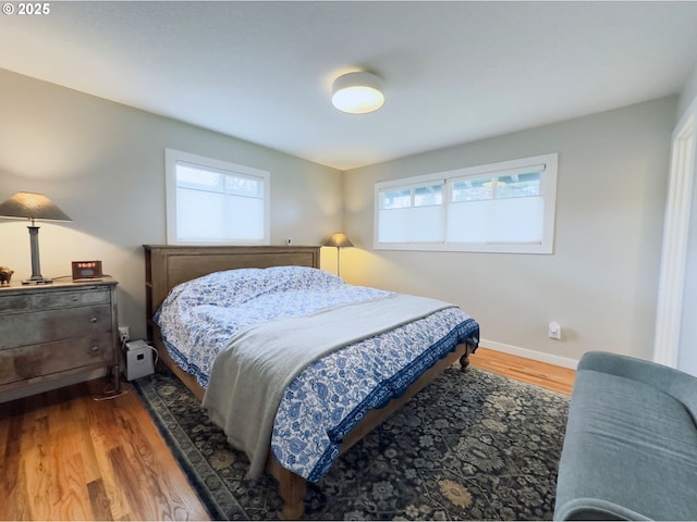 bedroom with baseboards, multiple windows, and wood finished floors