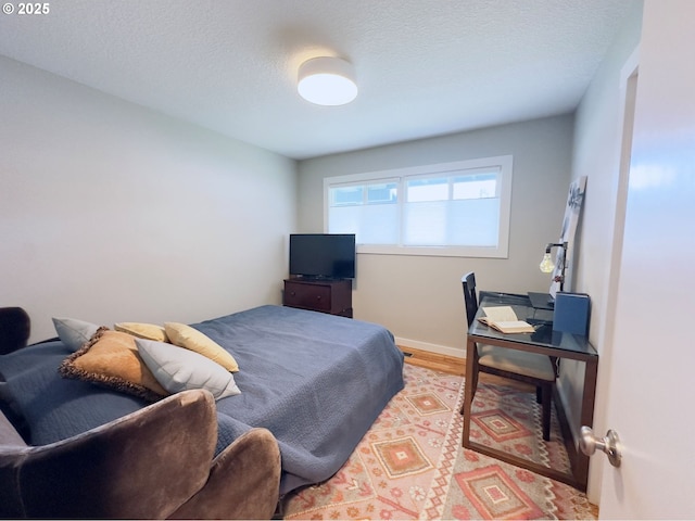 bedroom featuring light wood-type flooring, baseboards, and a textured ceiling