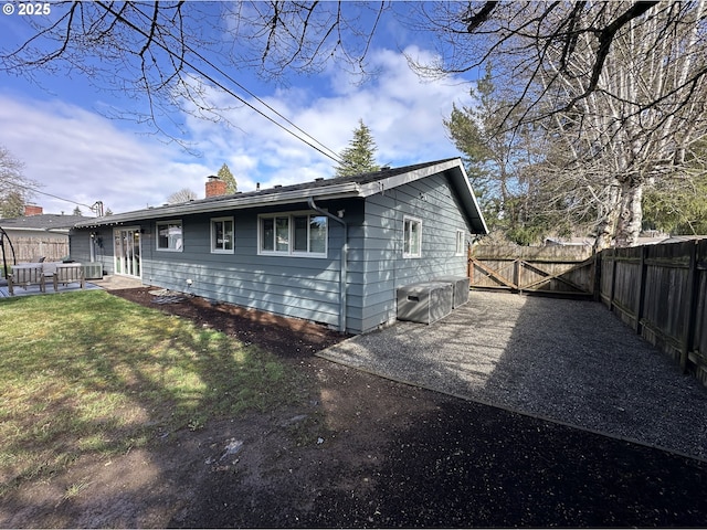 rear view of house with a lawn, a gate, fence, a chimney, and a patio area