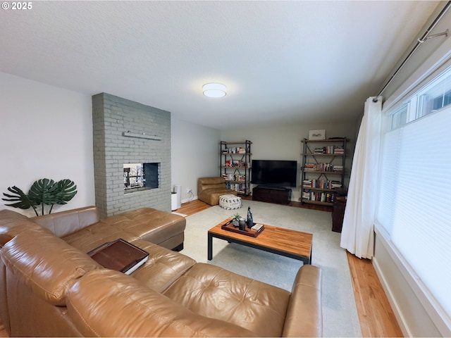 living area with a wealth of natural light, a brick fireplace, a textured ceiling, and light wood-type flooring