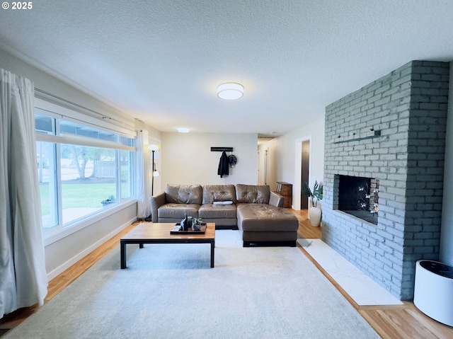 living room featuring a brick fireplace, wood finished floors, baseboards, and a textured ceiling