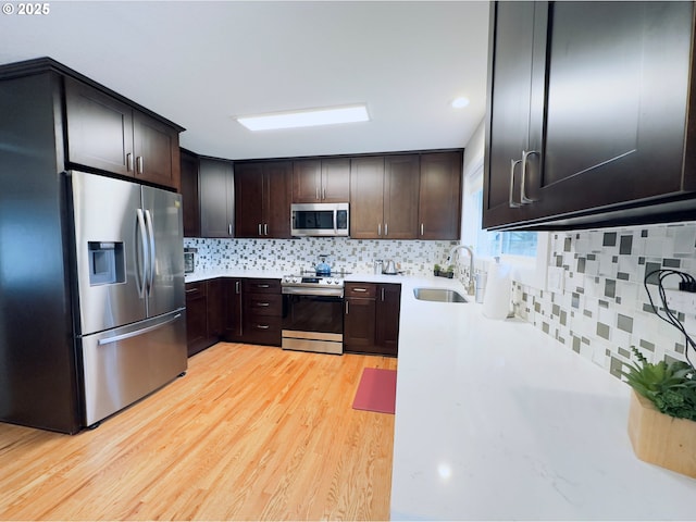 kitchen featuring a sink, stainless steel appliances, dark brown cabinetry, light wood finished floors, and light countertops