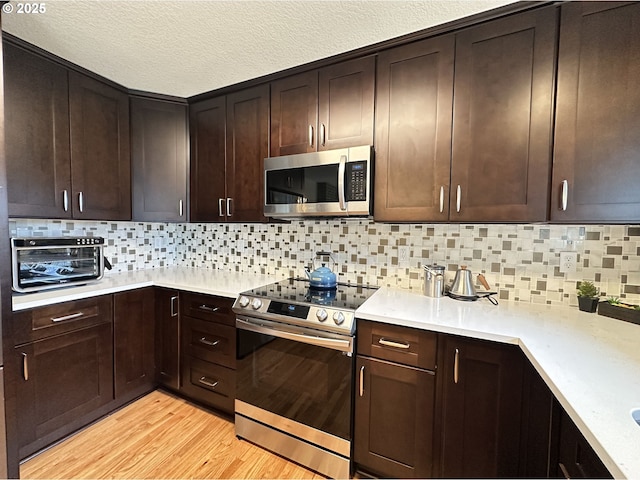 kitchen with light countertops, light wood finished floors, appliances with stainless steel finishes, and dark brown cabinets