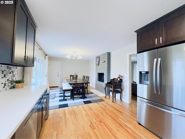 kitchen featuring light wood finished floors, light countertops, decorative backsplash, an inviting chandelier, and stainless steel fridge