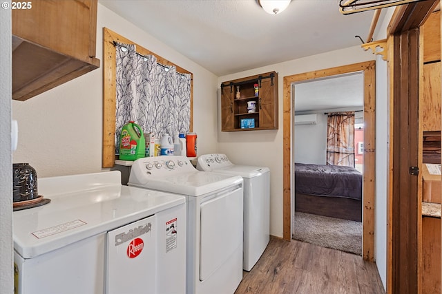 washroom with washing machine and clothes dryer, a wall unit AC, and light wood finished floors
