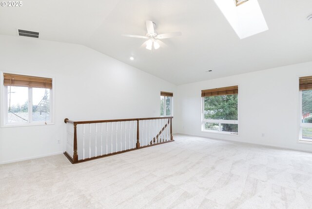 carpeted spare room featuring lofted ceiling with skylight, visible vents, a wealth of natural light, and ceiling fan