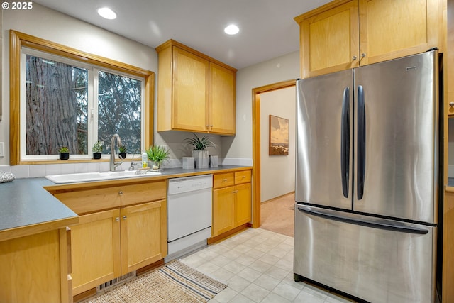 kitchen with recessed lighting, white dishwasher, freestanding refrigerator, light brown cabinetry, and a sink