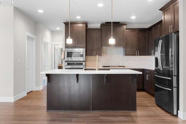 kitchen with decorative light fixtures, light wood-type flooring, stainless steel appliances, and a center island with sink