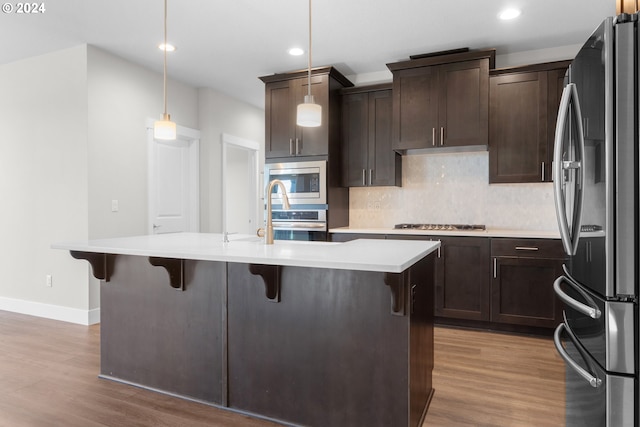 kitchen with appliances with stainless steel finishes, pendant lighting, wood-type flooring, and an island with sink