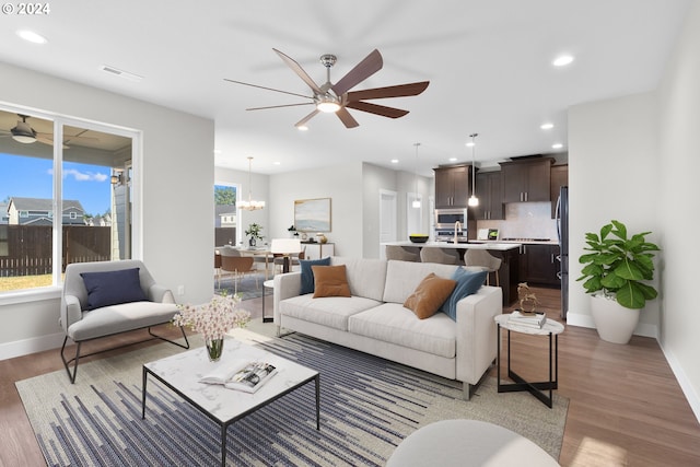 living room with ceiling fan with notable chandelier and hardwood / wood-style flooring