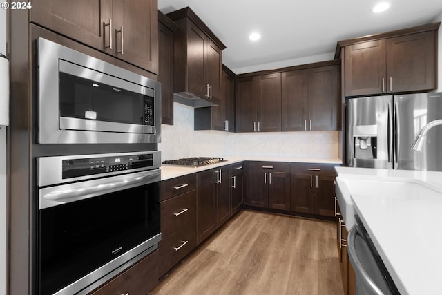 kitchen with tasteful backsplash, dark brown cabinetry, stainless steel appliances, and light wood-type flooring