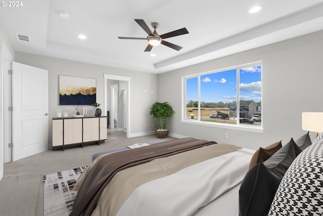 bedroom with ceiling fan, a tray ceiling, and light carpet