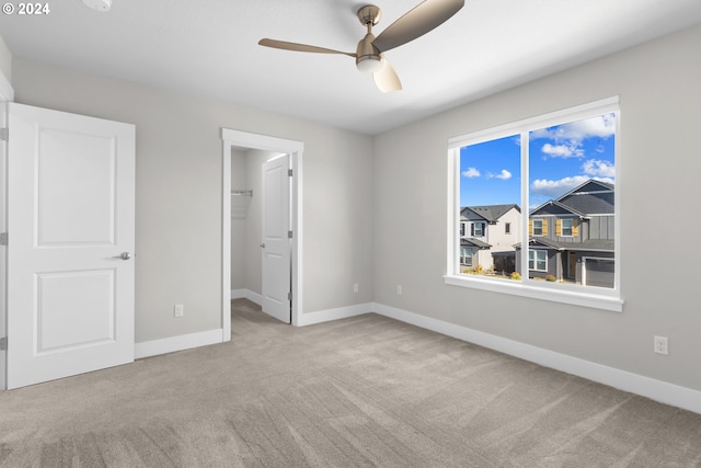 unfurnished bedroom featuring a spacious closet, a closet, light carpet, and ceiling fan