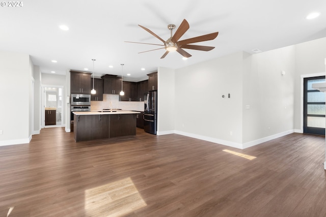 kitchen with stainless steel appliances, decorative light fixtures, a kitchen island with sink, dark wood-type flooring, and dark brown cabinets