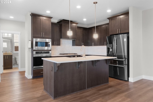 kitchen with decorative light fixtures, dark hardwood / wood-style flooring, stainless steel appliances, and an island with sink