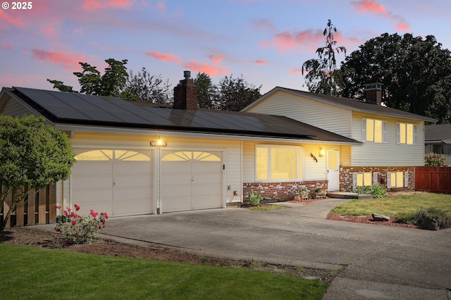 18735 NE Wasco Ct, Portland, OR 97230 - tri-level home with a chimney, solar panels, brick siding, an attached garage, and driveway