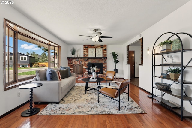 18735 NE Wasco Ct, Portland, OR 97230 - living area with ceiling fan, hardwood / wood-style flooring, a brick fireplace, baseboards, and a textured ceiling