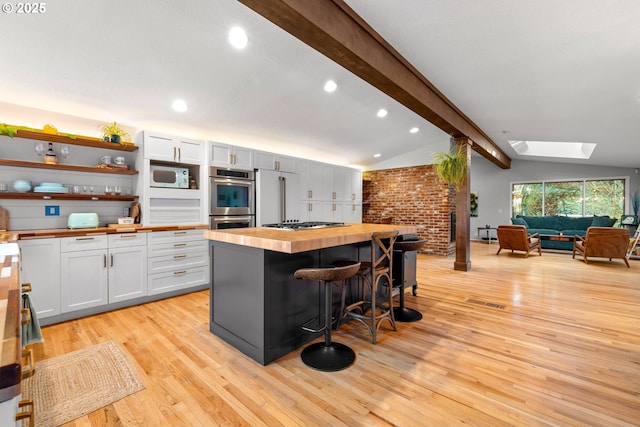 kitchen featuring vaulted ceiling with skylight, butcher block countertops, a breakfast bar, open floor plan, and appliances with stainless steel finishes