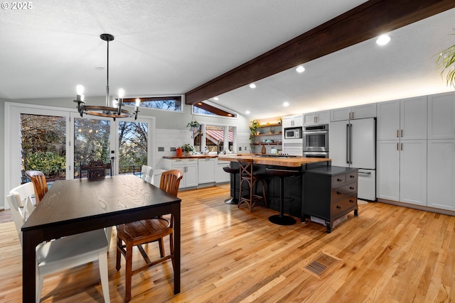 dining area featuring a chandelier, vaulted ceiling with beams, a textured ceiling, and light wood finished floors