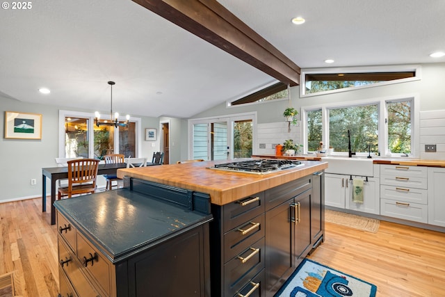 kitchen with vaulted ceiling with beams, stainless steel gas cooktop, butcher block countertops, a sink, and white cabinetry