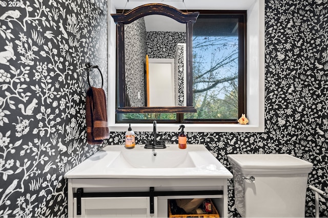 half bathroom with vanity, toilet, and wallpapered walls