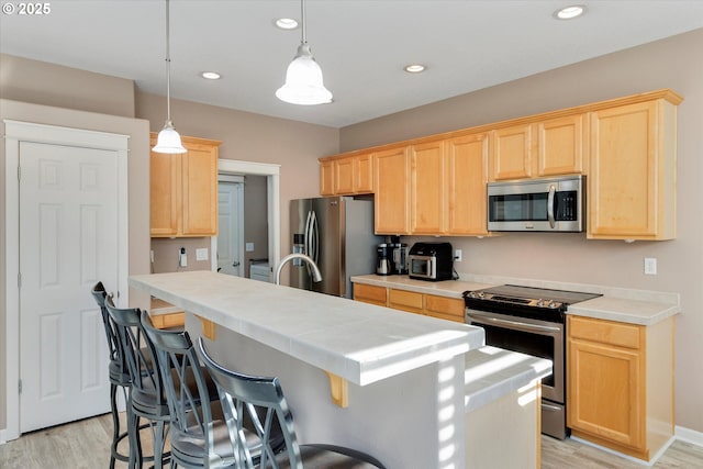 kitchen with light brown cabinets, pendant lighting, appliances with stainless steel finishes, light wood-type flooring, and an island with sink