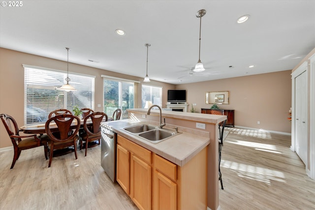 kitchen featuring light hardwood / wood-style flooring, dishwasher, sink, decorative light fixtures, and an island with sink