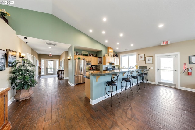 kitchen with dark wood-type flooring, kitchen peninsula, a breakfast bar, and stainless steel refrigerator